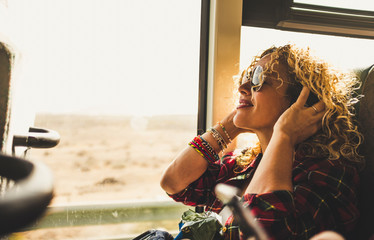 Beautiful blonde adult woman enjoying the travel on bus or train listening music with headphones - wanderlust lifestyle and happy people doing trip - happy people and transport