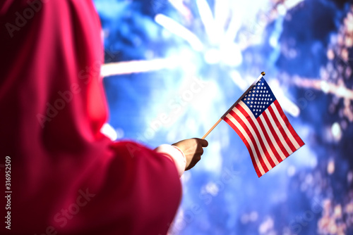 Muslim woman in a scarf holding American flag  during fireworks at night. photo