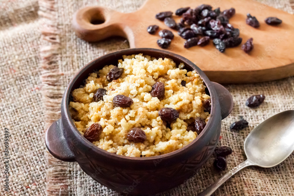 Sweet millet porridge with dark raisins in ceramic rustic bowl Sweet millet porridge with dark raisins in ceramic rustic bowl
