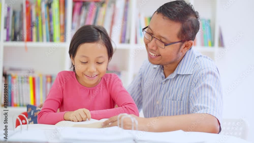 Young man helping his daughter to study and kiss her after reading book in the library. Shot in 4k resolution Young man helping his daughter to study and kiss her after reading book in the library. Shot in 4k resolution