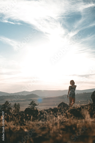 silhouette of a young girl at sunset, she stands on a hill scorched by the sun and looks towards high snowy mountains