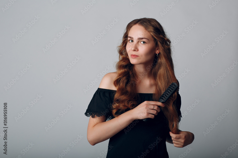 Portrait of woman with wavy hair combing with hairbrush on gray background Portrait of woman with wavy hair combing with hairbrush on gray background