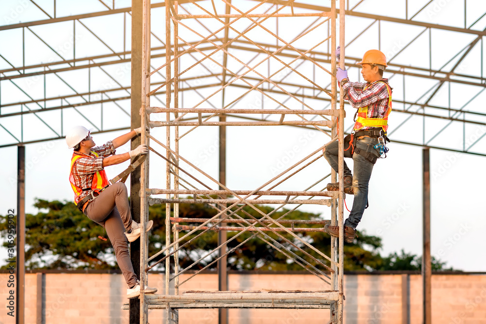 Fototapeta premium Technicians in safety clothing are climbing scaffolding. Friends go up and check the strength of the metal roof part of the building.