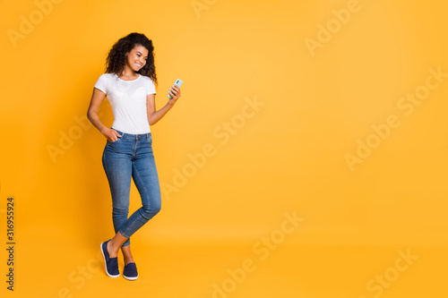 Full length body size photo of cheerful confident positive nice charming beautiful girl curly wavy wearing white t-shirt jeans denim footwear with hand pocket isolated over vivid color background