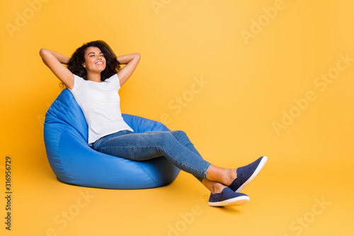 Portrait of her she nice attractive lovely charming cheerful cheey dreamy wavy-haired girl sitting in bag chair resting holiday isolated over bright vivid shine vibrant yellow color background