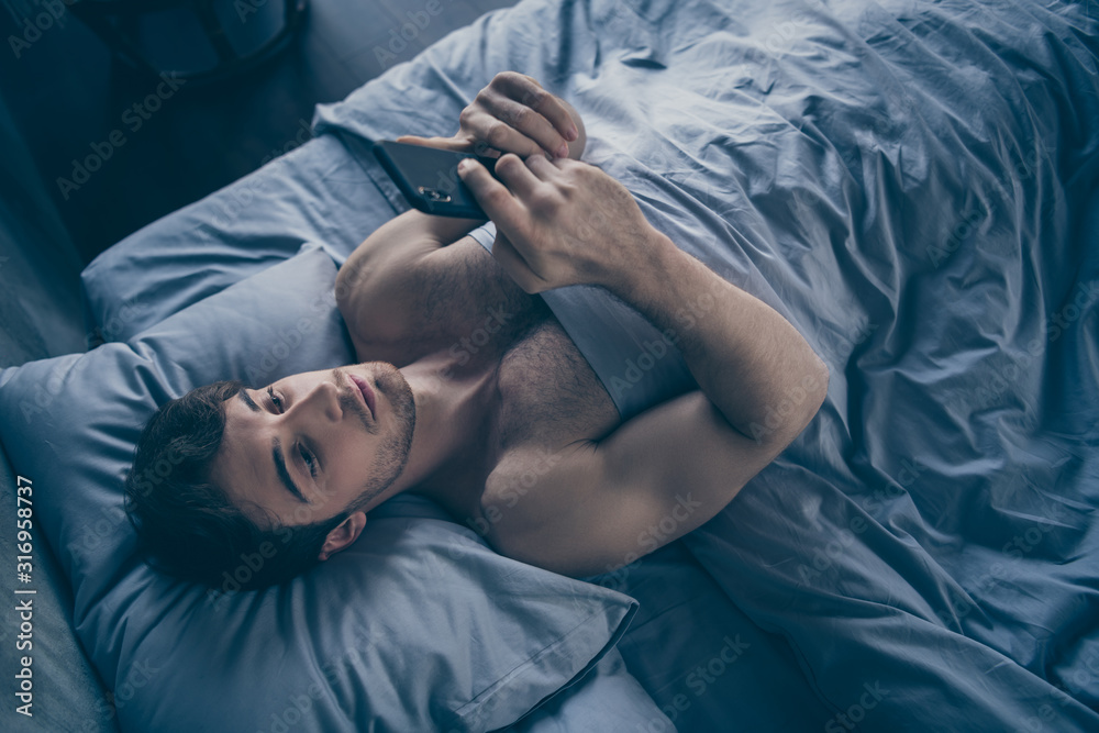 High angle above view photo of handsome homey macho guy lying morning bed alone holding telephone sending message lover mistress calling home visit him sheets room indoors High angle above view photo of handsome homey macho guy lying morning bed alone holding telephone sending message lover mistress calling home visit him sheets room indoors