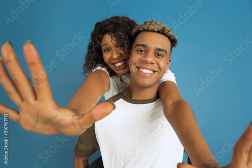 Young emotional african-american man and woman in white casual clothes posing on blue background. Beautiful couple. Concept of human emotions, facial expession, relations, ad. Hugging, laughting.
