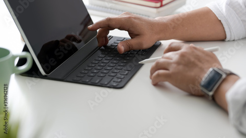 Cropped shot of businessman typing on tablet keyboard in simple workspace with coffee cup and office supplies