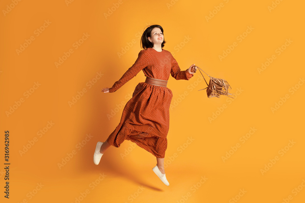 Beautiful woman jumping on yellow background with copy space. Studio shot of pretty girl in romantic summer dress