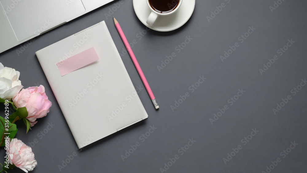Top view of workspace with notebook, laptop, coffee cup and flower vase on grey table