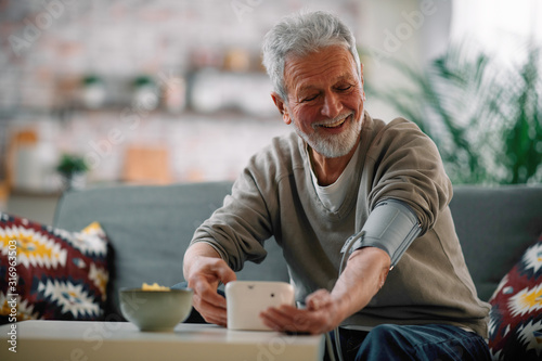 Old man sitting in living room. Happy senior man checking blood pressure. 