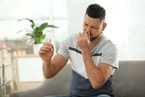 Emotional man with nicotine patch and cigarette at home photo