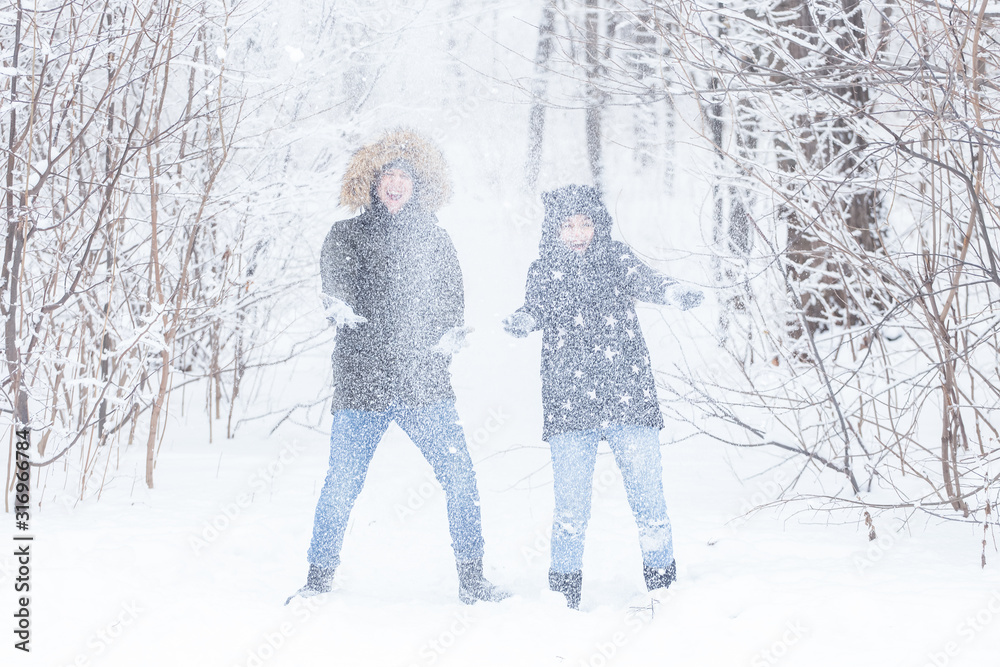 Love, relationship, season and friendship concept - man and woman having fun and playing with snow in winter forest
