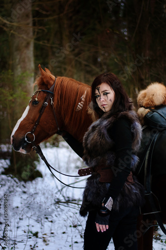 a Viking girl next to a red horse painted in black runes.