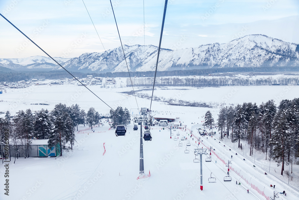 Landscape in Altay mountains with a gondola cableway booths suspended on a cable with skis and snowboards with snow on winter sunset. Ski resorts and snowboarding. Landscape in Altay mountains with a gondola cableway booths suspended on a cable with skis and snowboards with snow on winter sunset. Ski resorts and snowboarding.