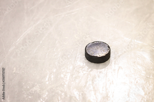 Black ice hocikey rubber puck located on arena ice rink. Ice and puck have small and deep scratches.