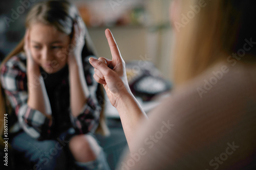 Mother scolding daughter. Scared girl covering ears .  photo