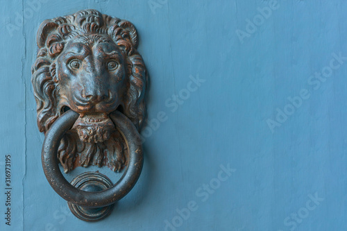 Old metal door handle in the shape of a lion's head with a ring in his mouth on a wooden background
