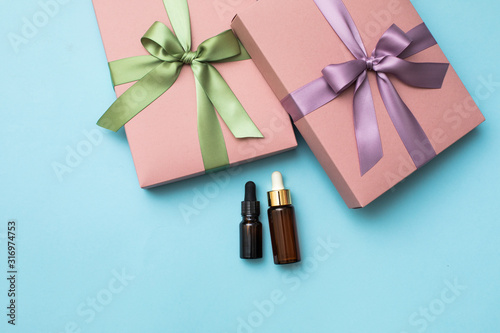 Pink gift box with ribbon and bow on blue background. Glass cosmetic bottle with dropper pipette.