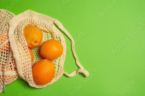 Eco friendly crochet shopping bag with oranges on green background with copy space. Zero waste food shopping concept. Plastic free items for stop pollution. Sustainable lifestyle concept