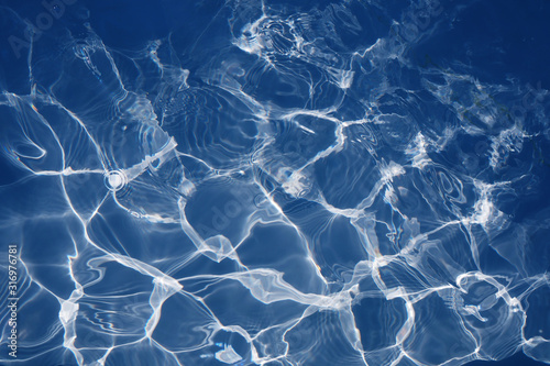 Water in swimming pool background for design. Blue water surface with bright sun light reflections