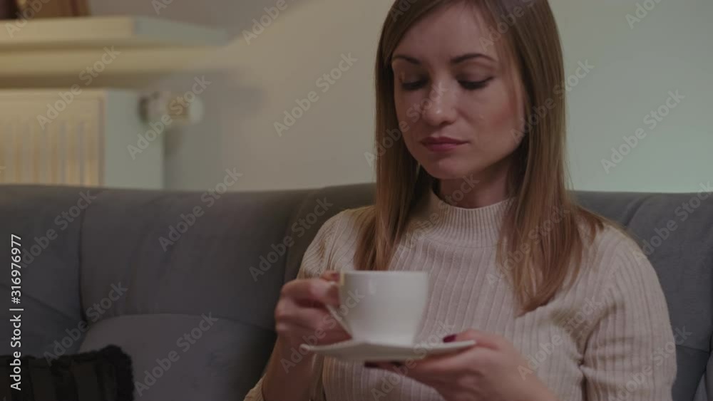 Portrait young woman drinking tea from white cup, while watching TV and sitting on the sofa in night. Panning shot Portrait young woman drinking tea from white cup, while watching TV and sitting on the sofa in night. Panning shot