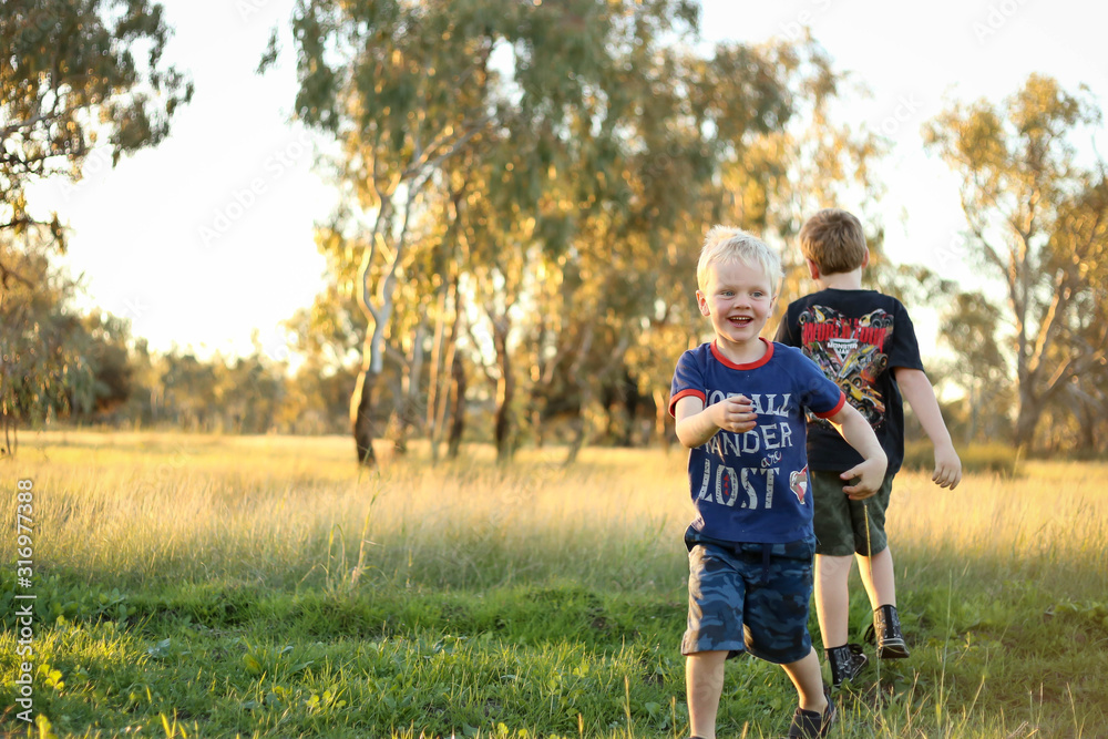 Fototapeta premium Little boys playing together in vibrant field at sunset with copy space