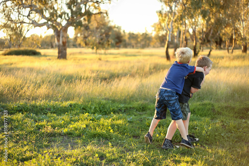 Little boy giving his little brother a piggy back. Boys playing together in vibrant field at sunset with copy space.