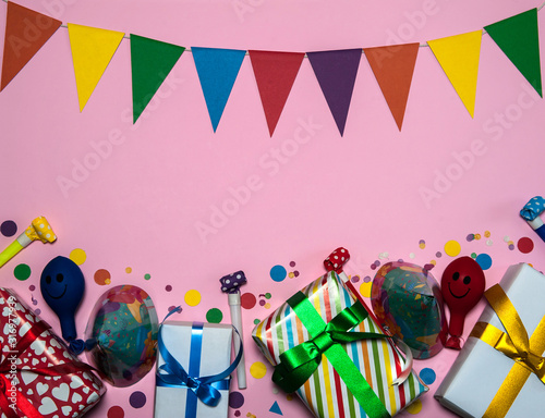 The concept of birthday. The frame is made of gift boxes, garlands of flags, confetti, cone-shaped caps, blowouts and balloons on a pink background. Free space.