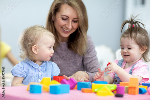 children toddlers playing with teacher in nursery or daycare