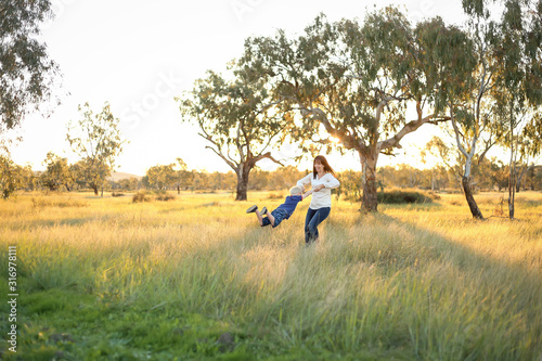 Mother and son playing together in a picturesque field with long grass at sunset. Family time. Mother-son bond. Beautiful image for mother's day with copy space. © Caseyjadew