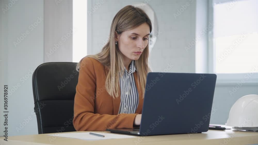 Intelligent and concentrated collar worker in formal wear clothes sitting behind table in modern coworking place with bright interior office. Woman using laptop and making notes on document Intelligent and concentrated collar worker in formal wear clothes sitting behind table in modern coworking place with bright interior office. Woman using laptop and making notes on document