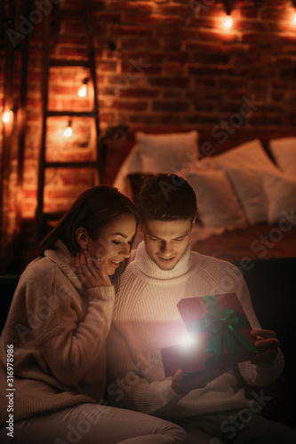 Handsome man presenting a gift to his beautiful girlfriend and smiling. Beautiful young couple at home enjoying spending time together.Valentine's Day, relationships and people concept.