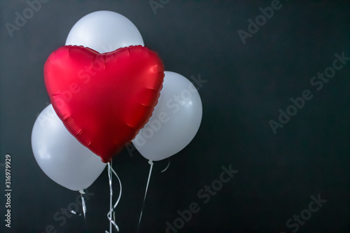 Red heart-shaped balloon and white round air balloons on a black background. Valentine s Day  holiday  love.