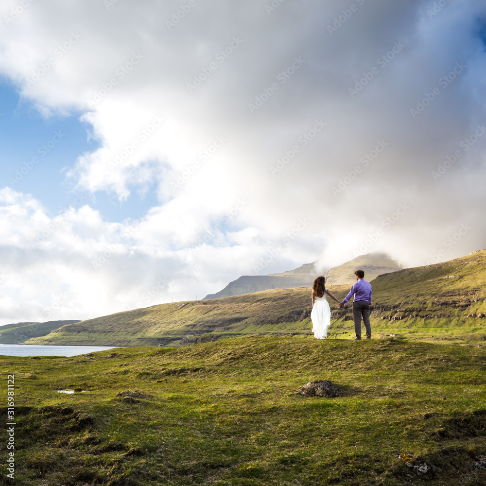A happy couple in wedding dresses or the bride and groom holding hands and looking at the picturesque nature. Faroe Islands