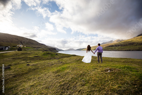 A happy couple in wedding dresses or the bride and groom holding hands and looking at the picturesque nature. Faroe Islands