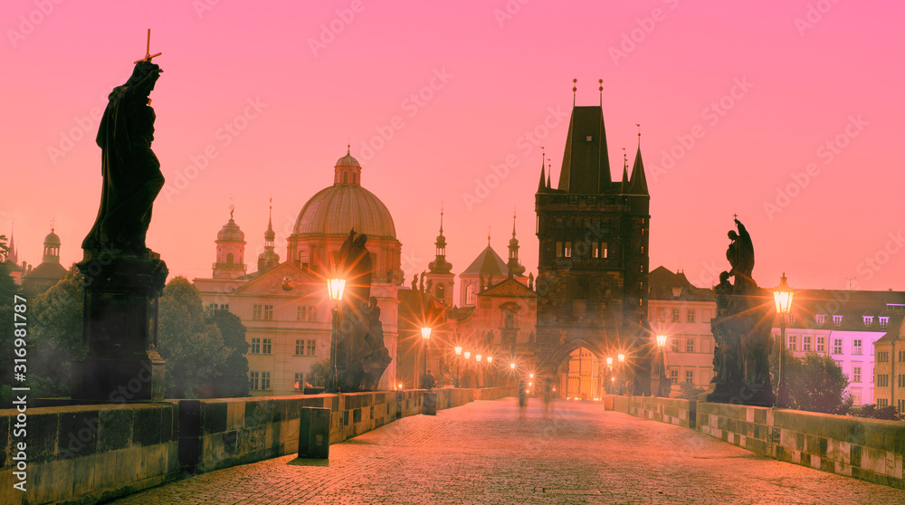 Charles Bridge in the morning, silhouette of Bridge Tower and saint sculptures with street lights in Prague, Czech Republic