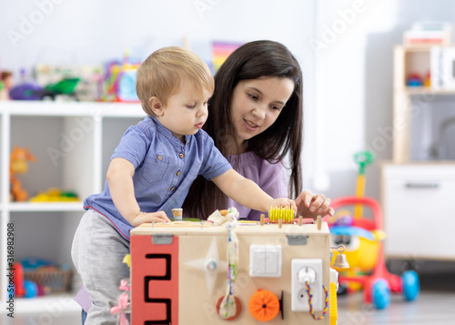 Cute toddler baby playing with busyboard. Mother teaching child in nursery or day care photo