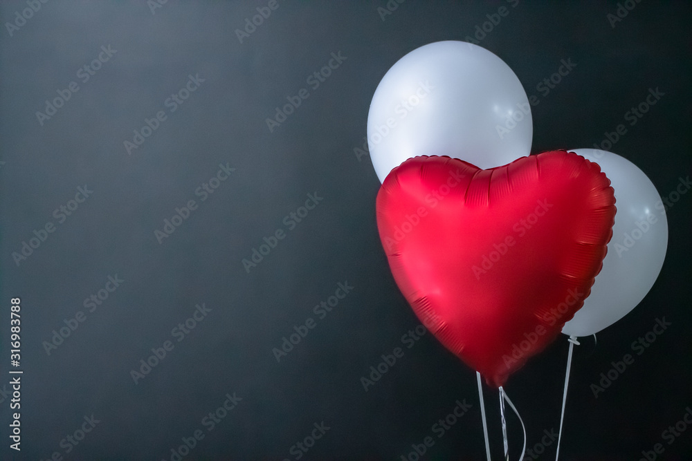 Red heart-shaped balloon and white round air balloons on a black background. Valentine's Day, holiday, love. Red heart-shaped balloon and white round air balloons on a black background. Valentine's Day, holiday, love.