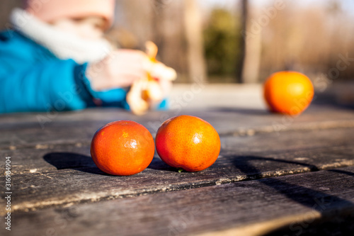 Kind schält Clemtine auf Holztisch im Herbst beim Wandern. Brotzeit. Child peeling clementine on wooden table after walking-tour.