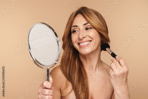 Portrait of smiling woman using powder brush and looking at mirror