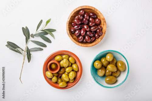 Different types of olives green and black in bowls on white table. Top view, close-up, copy space.