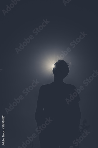 Silhouette of a person with sun behind causing sun eclipse effect. No colors. Dark and low angle image of someone unrecognizable.
