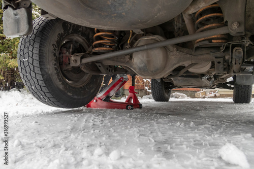 Car is lifted on a hydraulic Jack. Trolley Jack Car Lift and Jack stand for changing car wheels. Snowy background