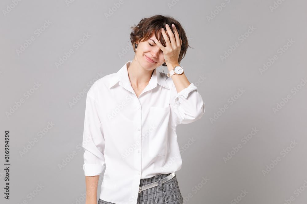 Young business woman in white shirt posing isolated on grey wall background studio portrait. Achievement career wealth business concept. Mock up copy space. Keeping eyes closed, putting hand on face. Young business woman in white shirt posing isolated on grey wall background studio portrait. Achievement career wealth business concept. Mock up copy space. Keeping eyes closed, putting hand on face.