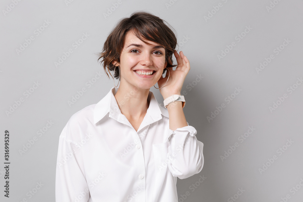 Smiling charming pretty young business woman in white shirt posing isolated on grey wall background studio portrait. Achievement career wealth business concept. Mock up copy space. Looking camera. Smiling charming pretty young business woman in white shirt posing isolated on grey wall background studio portrait. Achievement career wealth business concept. Mock up copy space. Looking camera.
