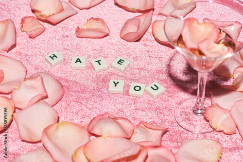 selective focus rose petals scattered near hate you lettering and glass on velour pink cloth, girlish concept