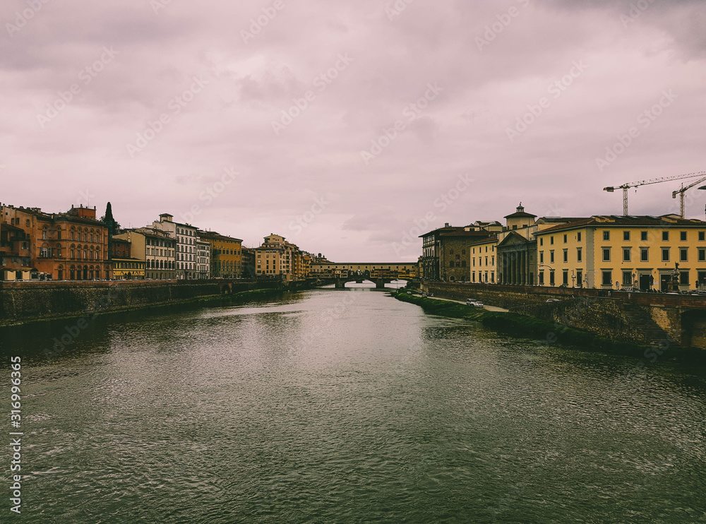 Ponte Vecchio and surrounding buildings in Florence shot from a bridge on a cloudy day.