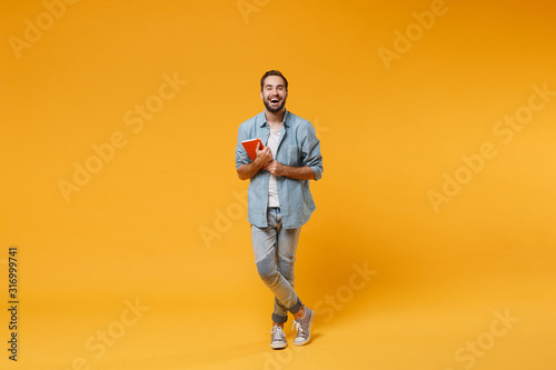 Laughing young student man in casual blue shirt posing isolated on yellow orange wall background studio portrait. People sincere emotions lifestyle concept. Mock up copy space. Holding red notebook.