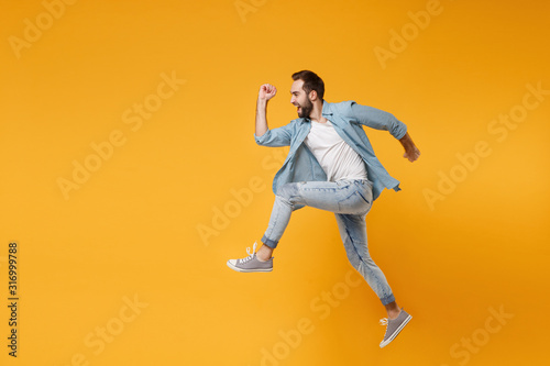 Side view of funny young bearded man in casual blue shirt posing isolated on yellow orange background studio portrait. People sincere emotions lifestyle concept. Mock up copy space. Jumping  running.